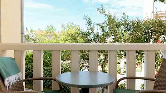 Två stolar och ett bord på en balkong med utsikt över grönska (AI-genererad text)