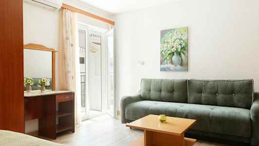 En ljus inomhusmiljö med en grön soffa, ett litet träbord och en spegel ovanpå ett skrivbord. En målning av blommor hänger på väggen. (AI-genererad text)