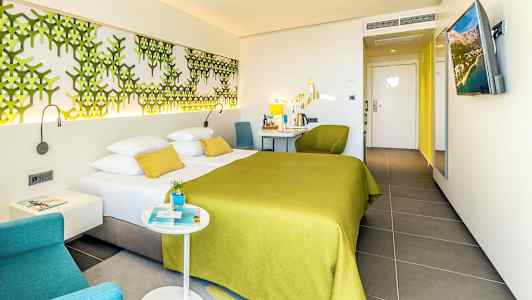 Ett hotellrum med en dubbelsäng med grön överkast och moderna möbler. (AI-genererad text)