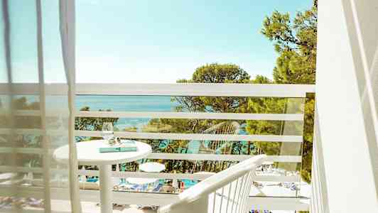 Utsikt från en balkong över en pool och havet med träd i förgrunden. (AI-genererad text)