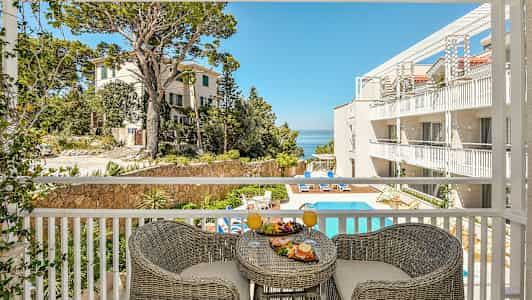 Utsikt från en balkong över en hotellpool och byggnader, med frukost serverad på ett bord. (AI-genererad text)