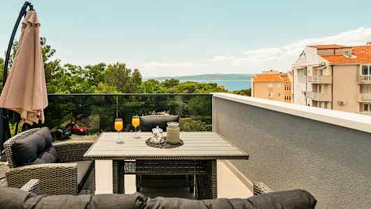 Terrass med bord och stolar, orange drycker i glas, paraply och utsikt över träd, byggnader och hav. (AI-genererad text)