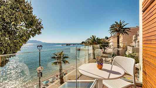 Utsikt från en balkong mot en solig strand med palmer och klart vatten. (AI-genererad text)