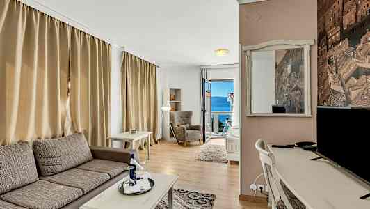 Ett rum med sittmöbler, skrivbord, och utsikt mot havet genom en öppnad dörr. (AI-genererad text)