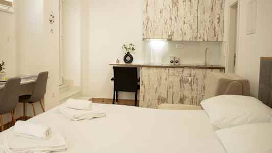 Bild av ett ljust inrett rum med säng, köksbänk och bord med stolar. (AI-genererad text)