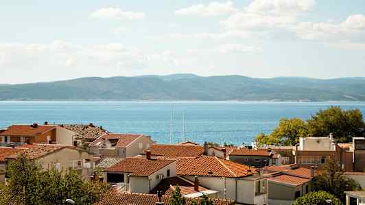 Röda tak på hus med havet och kullar i bakgrunden. (AI-genererad text)