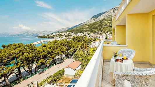 Utsikt från en gul byggnads balkong över en stad vid havet och omgivande berg. (AI-genererad text)