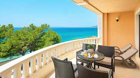 En balkong med utsikt över havet, sittgrupp och två solstolar. (AI-genererad text)