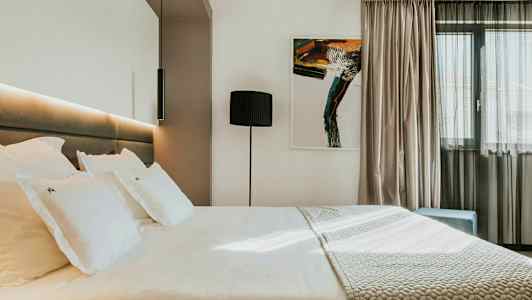 Modern hotellrum med en stor säng, konstverk på väggen och en fönster med ljusa gardiner. (AI-genererad text)