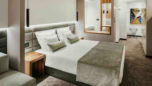 Ett modernt hotellrum med en stor säng, vit sängkläder, grå överkast och kuddar och ett grått heltäckningsmatta. (AI-genererad text)