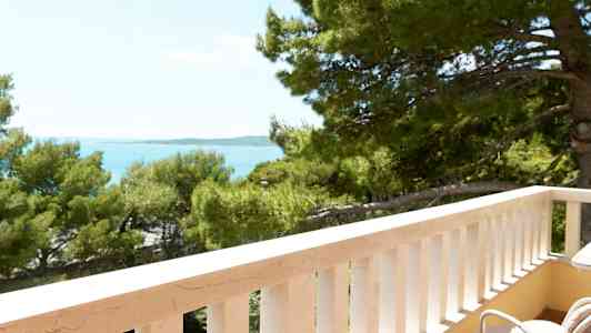 Utsikt från en balkong med vita räcken mot träd och hav. (AI-genererad text)
