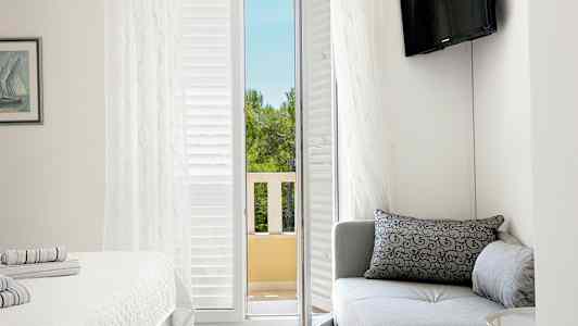 Ett hotellrum med en soffa, en säng och en balkongdörr som leder ut till en utsikt över träd. (AI-genererad text)