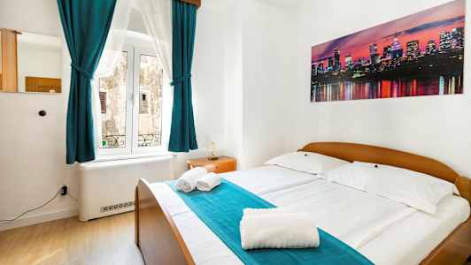 Ett sovrum med dubbelsäng, turkosa gardiner och en bild av en stadssiluett på väggen. (AI-genererad text)