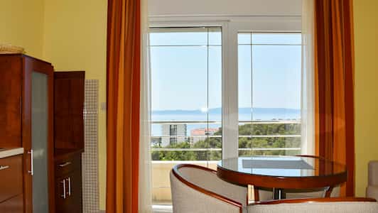 Ett rum med stora fönster som vetter mot en havsutsikt, med möbler inklusive ett runt bord och stolar. (AI-genererad text)