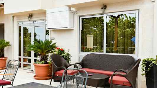 Uteplats med sittgrupp, gröna växter i krukor och glasdörrar. (AI-genererad text)