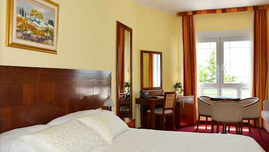 Ett hotellrum med en dubbelsäng, skrivbord, stolar och ett fönster. (AI-genererad text)