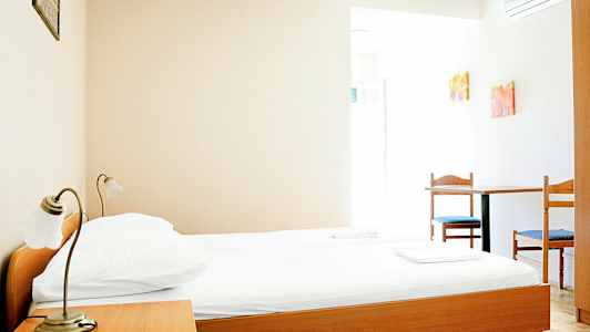 Ett enkelt hotellrum med en säng av trä, ett sängbord, och ett bord med två stolar. (AI-genererad text)