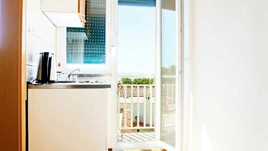 Ett litet kök med utsikt mot en balkong och havet i bakgrunden. (AI-genererad text)