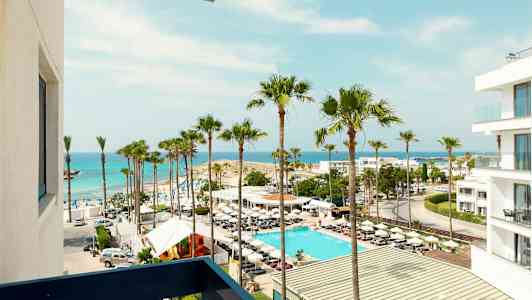 Vy över en strand med palmer, en pool och vit byggnad vid havet. (AI-genererad text)