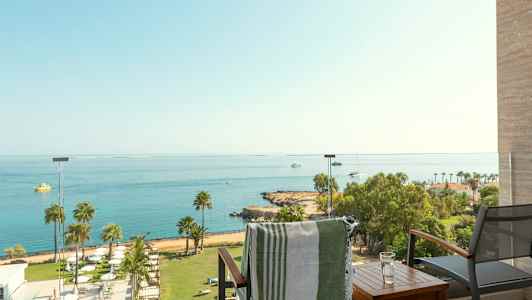 Utsikt från en balkong över ett hav med båtar och en strand med palmer. (AI-genererad text)