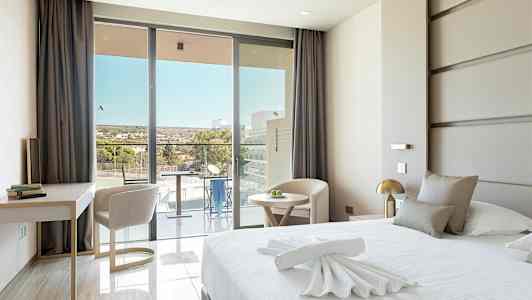 Ett modernt hotellrum med en stor säng, ett skrivbord och stolar, samt en balkong med utsikt. (AI-genererad text)