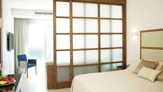 Hotellrum med säng och sittgrupp samt utsikt mot havet. (AI-genererad text)