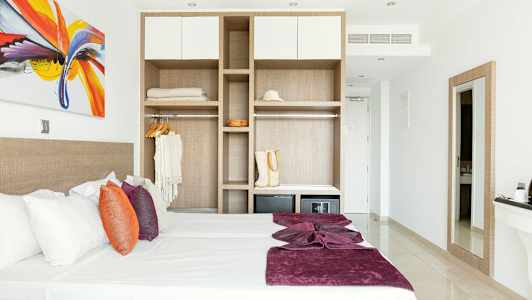 Modernt inrett hotellrum med säng, färgglada kuddar och öppen garderob. (AI-genererad text)