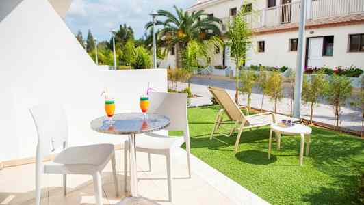 Utemöbler på en terrass med två färgglada drinkar, och en gräsmatta med solstol i bakgrunden. (AI-genererad text)