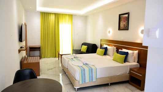 Ett hotellrum med två bäddade sängar, färgglada kuddar, en liten sittgrupp och limegröna gardiner. (AI-genererad text)