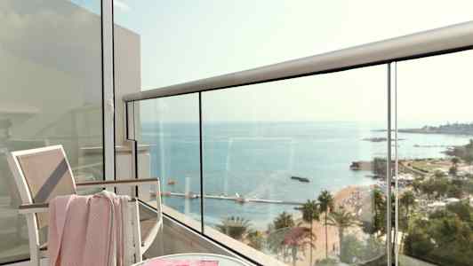 Utsikt från en balkong mot havet, med en stol, ett bord och ett magasintidning. (AI-genererad text)