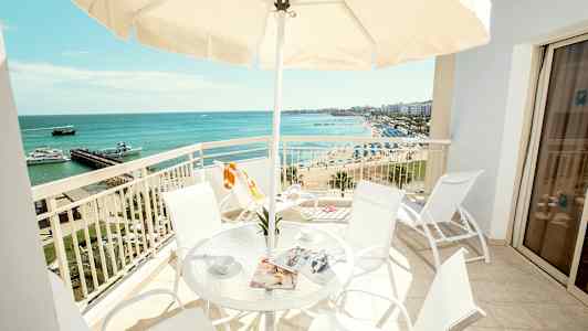 En balkong med bord och stolar, utsikt över stranden och havet. (AI-genererad text)