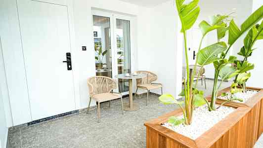 En uteplats med två stolar och ett bord, omgiven av gröna växter. (AI-genererad text)