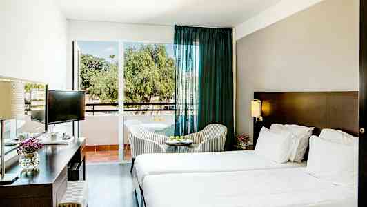 Hotellrum med två sängar, ett skrivbord och ett litet bord med stolar framför en glasdörr. (AI-genererad text)