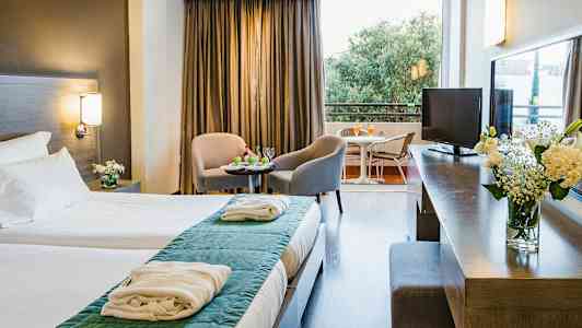 Ett hotellrum med dubbelsäng, sittgrupp med två stolar och bord, samt en balkong med utsikt. (AI-genererad text)