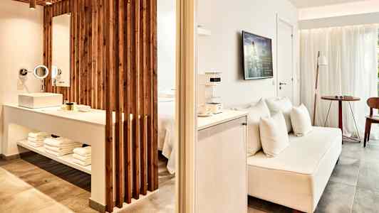 Ett hotellrum med öppen planlösning, inklusive en tv, en soffa och en del med handfat och badrumstillbehör. (AI-genererad text)