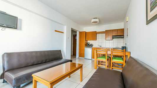 En interiör med två bruna soffor, ett glasbord och en köksdel med träskåp och matplats. (AI-genererad text)