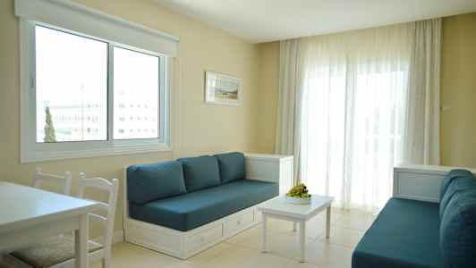 Ett rum med två soffor med blå kuddar, ett vitt bord och ett stort fönster försedd med vita gardiner. (AI-genererad text)