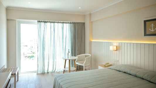 Bild av ett ljust hotellrum med en säng, ett bord och en stol nära ett fönster som har ljusa gardiner. (AI-genererad text)