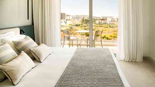 Hotellrum med en dubbelsäng och utgång till balkong med bord och stolar. (AI-genererad text)