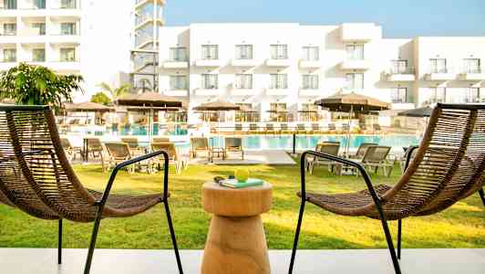 Två stolar och ett bord på en uteplats med utsikt över poolområdet och ett hotell. (AI-genererad text)