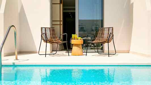 Två stolar och ett bord med glas står vid swimmingpoolen framför en dörr. (AI-genererad text)