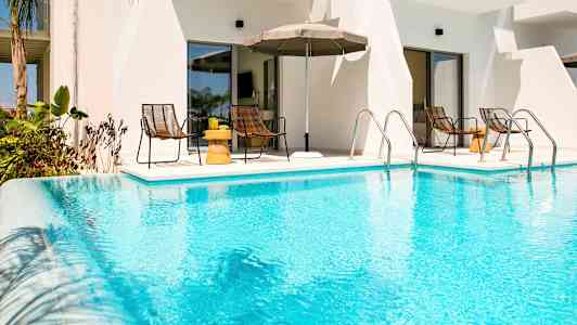 En utomhuspool framför en byggnad med bord och stolar i bakgrunden. (AI-genererad text)