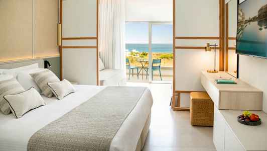 Ett hotellrum med en stor säng, TV, och utsikt över havet från en balkong. (AI-genererad text)