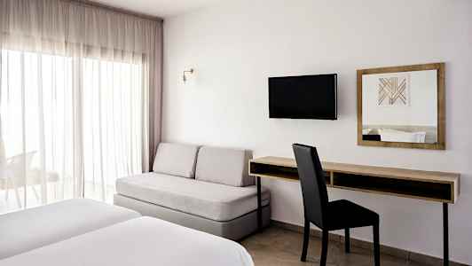 Ett hotellrum med två sängar, en soffa, ett skrivbord och en väggmonterad TV. (AI-genererad text)