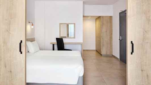 Ett hotellrum med en dubbelsäng, skrivbord, spegel och förvaringsmöbler. (AI-genererad text)