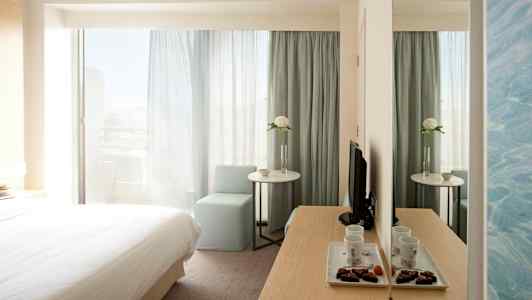 Hotellrum med säng, bord, stol och spegel. (AI-genererad text)