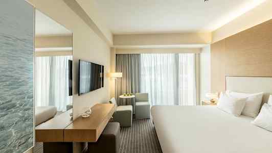 Hotellrum med en stor säng, TV på väggen och sittgrupp vid fönstret. (AI-genererad text)