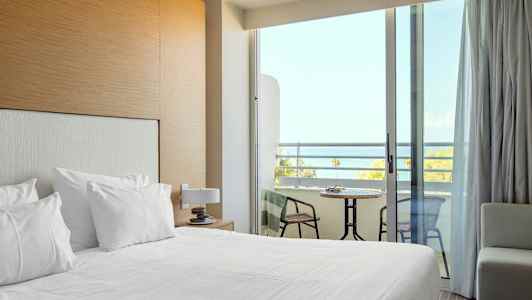 Ett hotellrum med bäddad säng och en balkong med utsikt över havet. (AI-genererad text)
