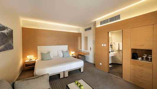 Ett modernt hotellrum med en dubbelsäng, en sittgrupp och ett skrivbord. Till höger finns en garderob och en dörr som leder till ett badrum. (AI-genererad text)