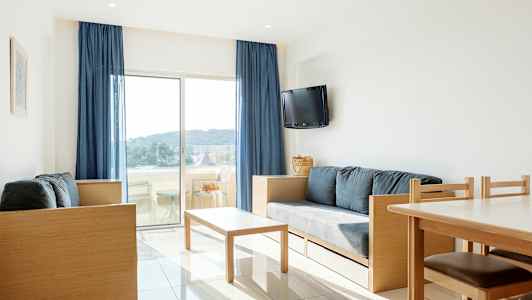 Ett ljust vardagsrum med moderna möbler och utsikt över en balkong med landskap utanför. (AI-genererad text)